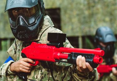 Paintball player holding a pump action paintball gun while wearing a mask