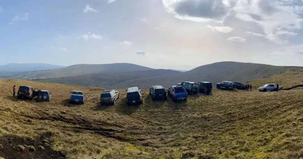 Row of SUVs and pick up trucks staring out a mountain range from a mountain peak
